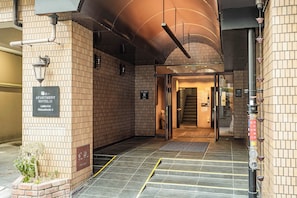 A hotel entrance with a brick facade, a sign indicating the name and location, and a staircase leading to the interior. - Apartment Hotel 11 Shinsaibashi 4 (Osaka)
