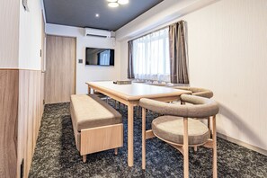 A compact room with a wooden table, two chairs, a bench, a television, and a window with curtains. - Apartment Hotel 11 Shinsaibashi 4 (Osaka)