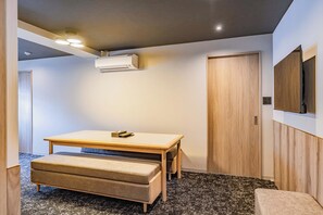 Ein kleines Zimmer mit einem Holztisch, einer Bank und einer Wandklimaanlage.