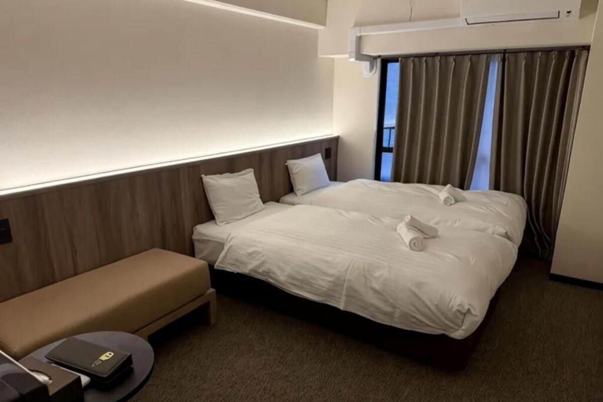 A hotel room with a bed, a sofa, a small table, and a window with curtains.
