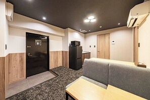 Ein kleines Hotelzimmer mit einer Küchenzeile, einem Sofa, einem Tisch und einer Tür zu einem weiteren Raum.