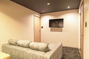 A room with a sofa, a television mounted on the wall, and a door. - Apartment Hotel 11 Shinsaibashi 4 (Osaka)