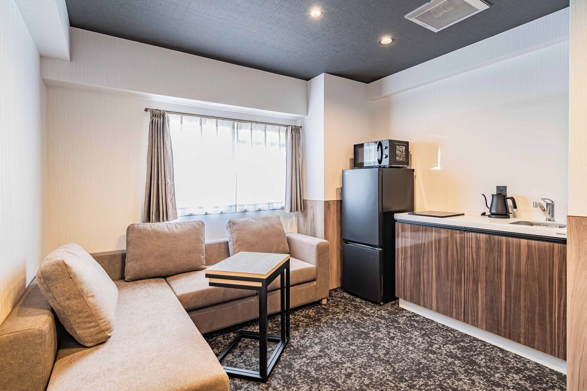 A compact living space with a sofa, a small table, a refrigerator, and a kitchenette area.
