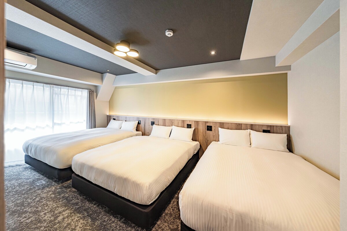 A hotel room with two beds, a large window with curtains, and a ceiling with recessed lighting.