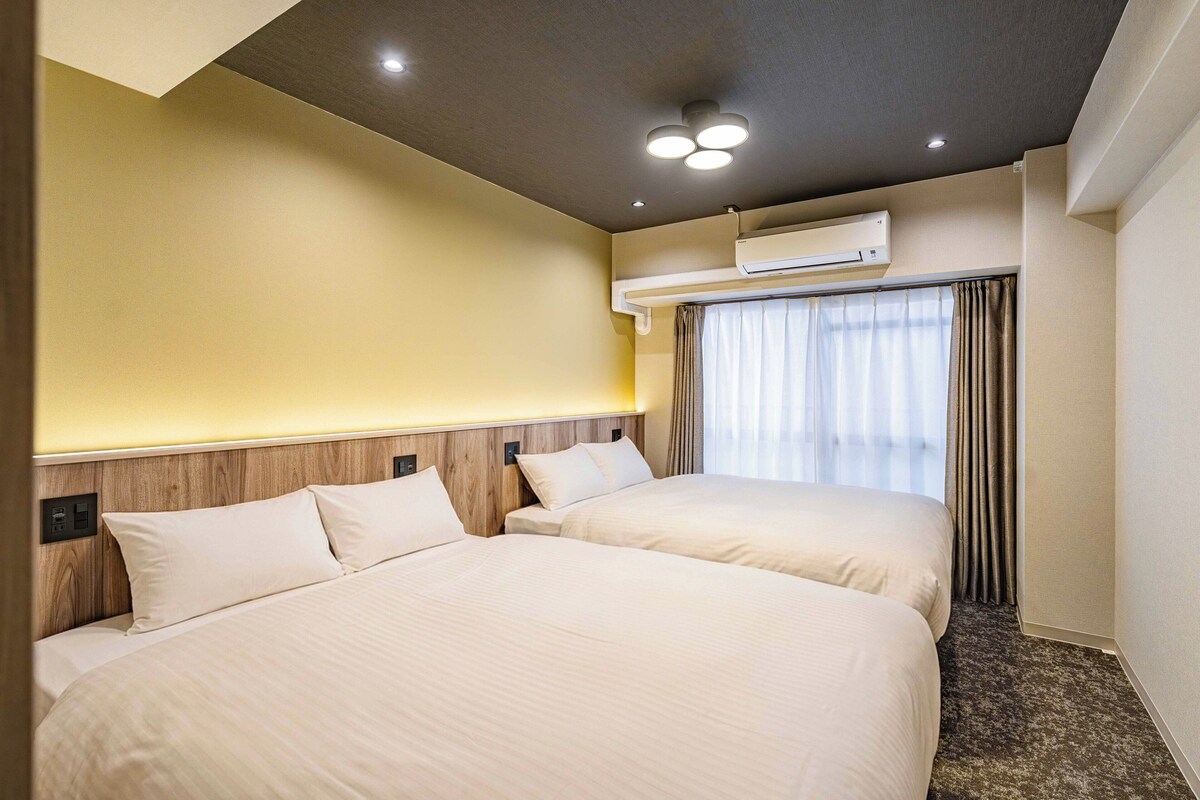 A hotel room with two beds, an air conditioning unit, and a window with curtains.
