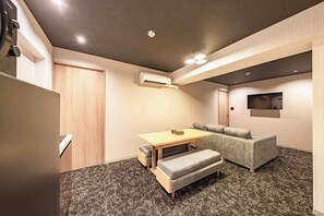 Un espacio habitable compacto con una puerta de madera, una mesita con cojín, un sofá gris y un televisor de pantalla plana montado en la pared.