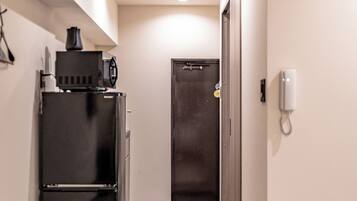 A narrow hallway with a kitchenette on the left, a door at the end, and a phone on the wall.