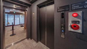 An elevator with a digital display, emergency exit sign, and a no-smoking sign. - Apartment Hotel 11 Namba Minami Shin-Imamiya (Osaka)