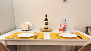 Ruokapöytä on katettu: siellä on lautasia, aterimia, viinipullo, laseja ja pientä naposteltavaa.