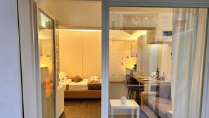 Moderni hotellihuone, jossa on sänky, pieni pöytä sekä oleskelualue, jossa on sohva ja tuoleja.