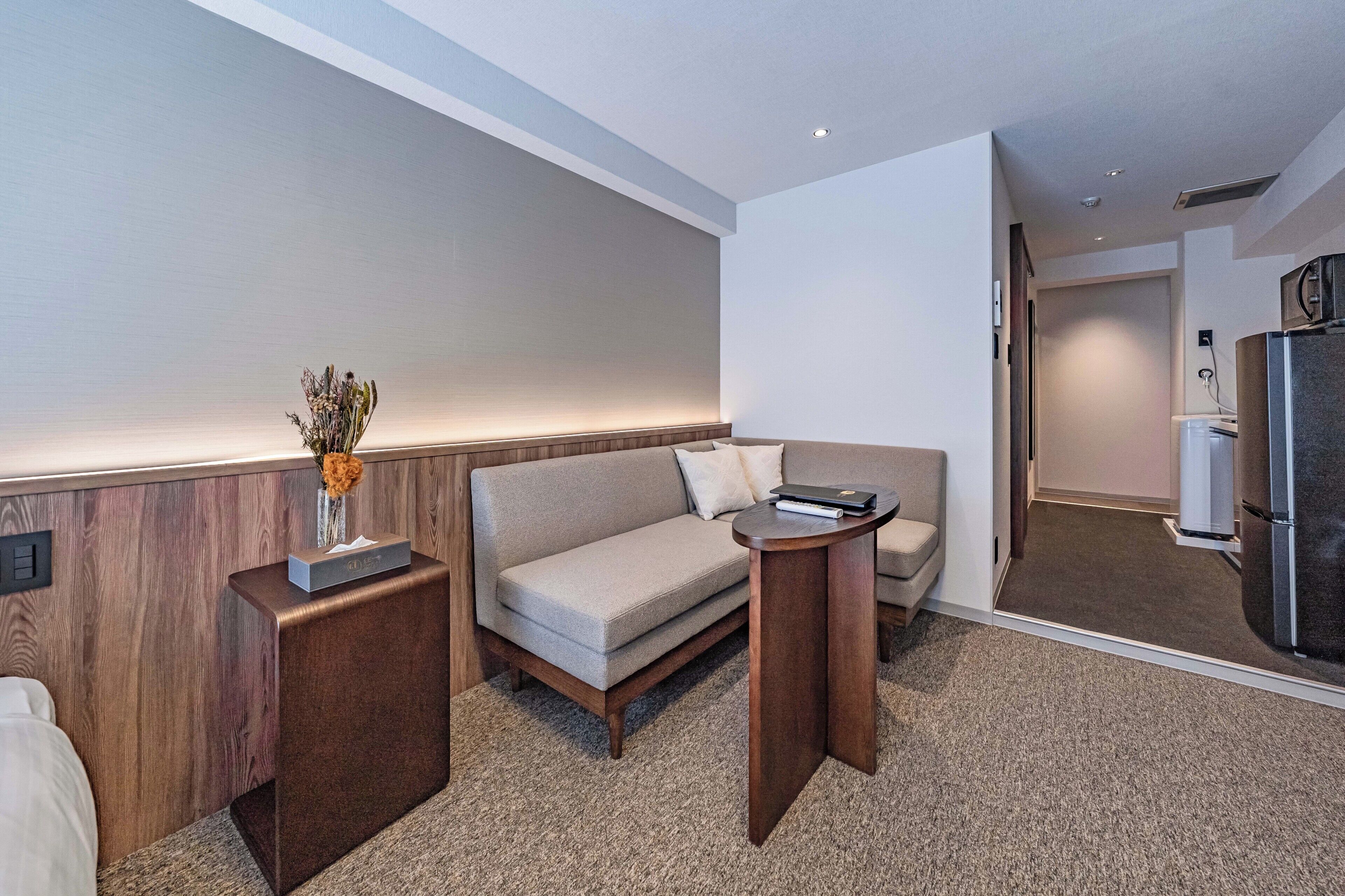 A hotel room with a sofa, a small table, a vase with dried flowers, and a minibar.