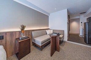 A hotel room with a sofa, a small table, a vase with dried flowers, and a minibar.