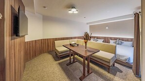 A hotel room with a sofa, a small table, a vase with dried flowers, and a bed with a white comforter. - Apartment Hotel 11 Shinsaibashi 5 (Osaka)