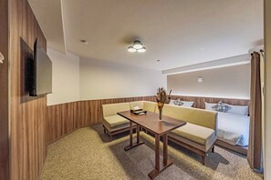Une chambre d’hôtel avec un canapé, une petite table, un vase contenant des fleurs séchées et un lit recouvert d’une couette blanche.