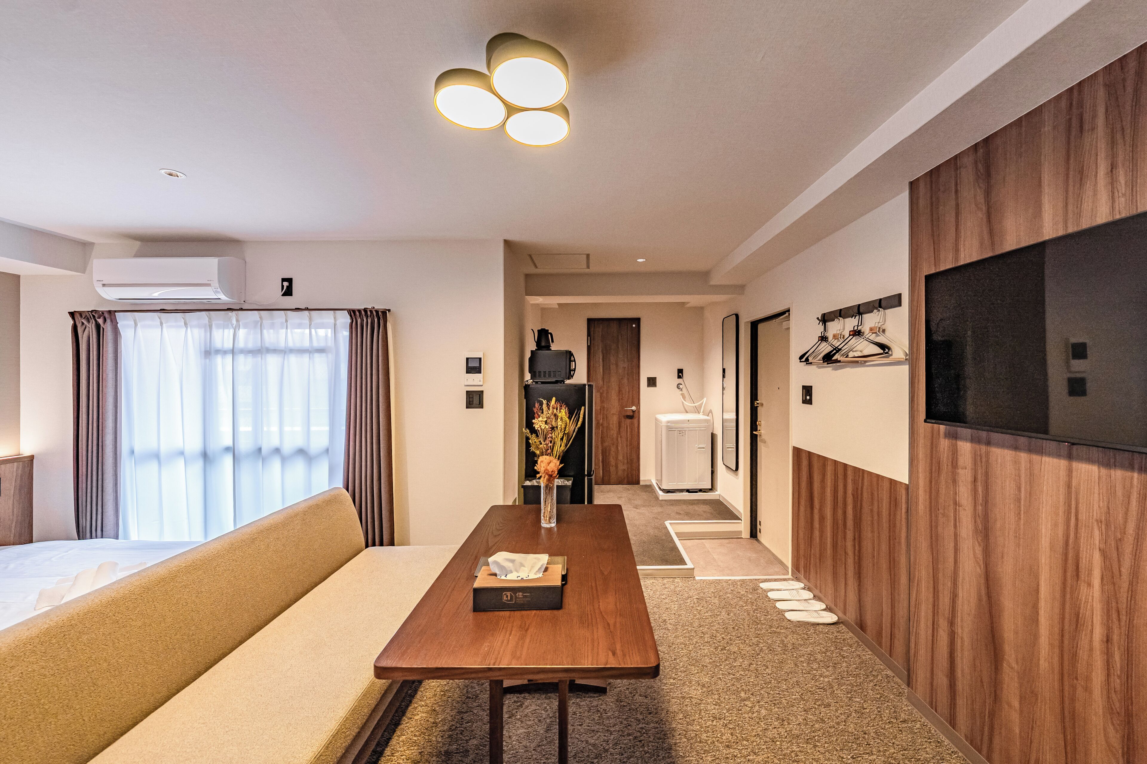 A hotel room with a sofa, a wooden table, a TV, and a minibar.