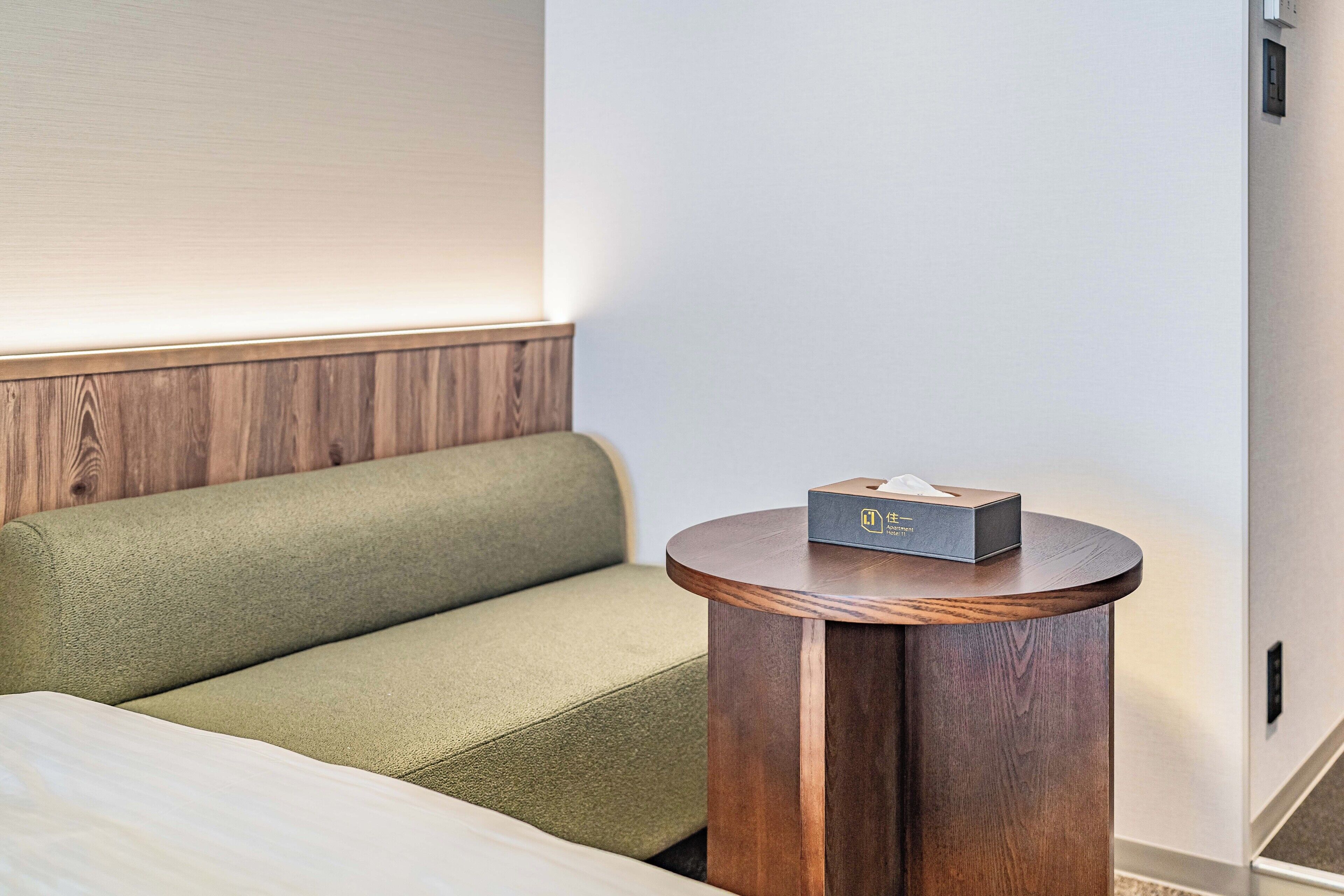A hotel room with a green sofa, a wooden side table, and a tissue box on the table.
