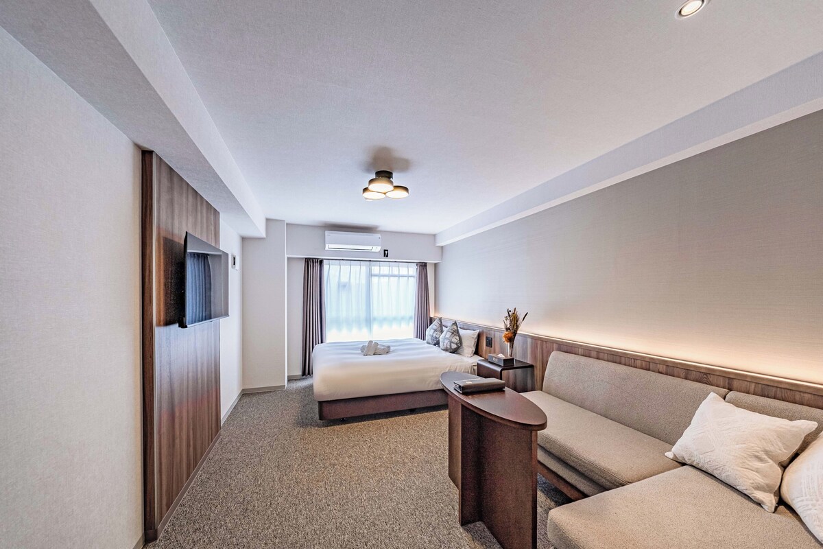 A hotel room with a bed, a sofa, a desk, and a TV.