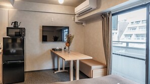 Ein kleines Hotelzimmer mit Küchenzeile, einem Esstisch, einer Bank und einem großen Fenster mit Blick auf die Stadt.