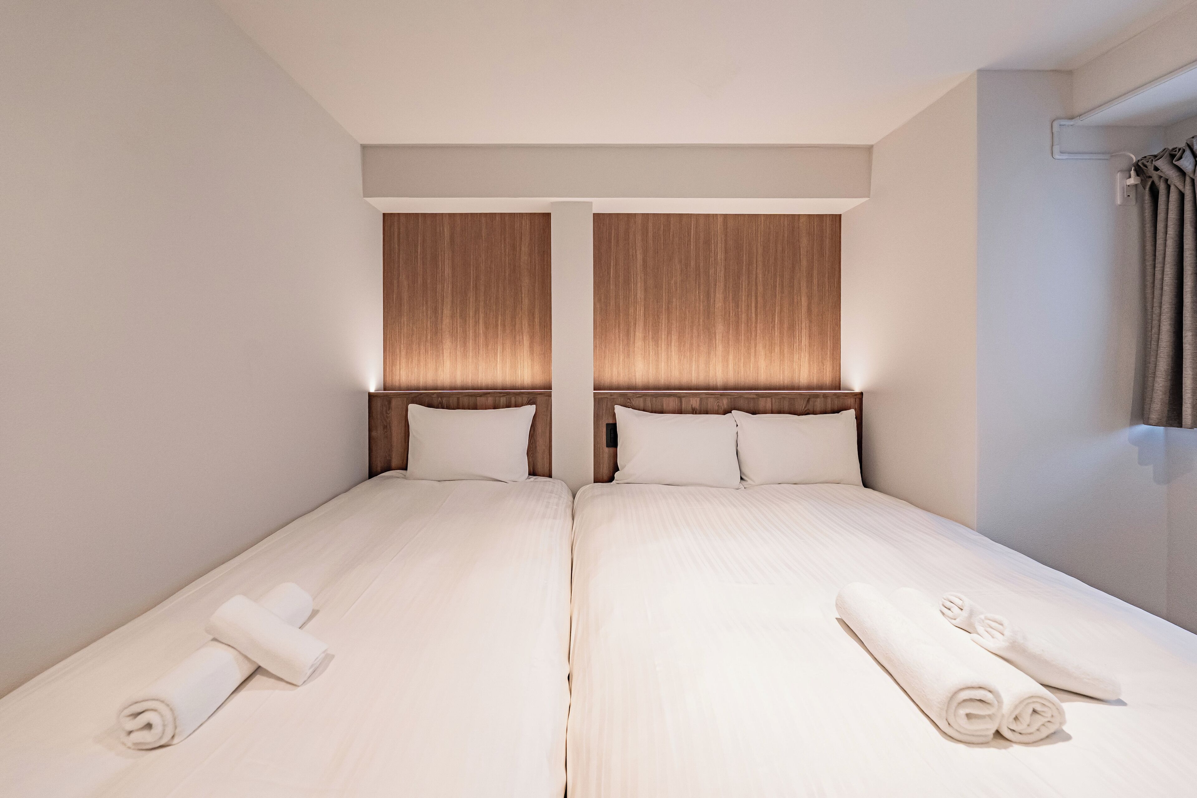 A double room with two beds, each with a wooden headboard, white linens, and rolled towels on the side.