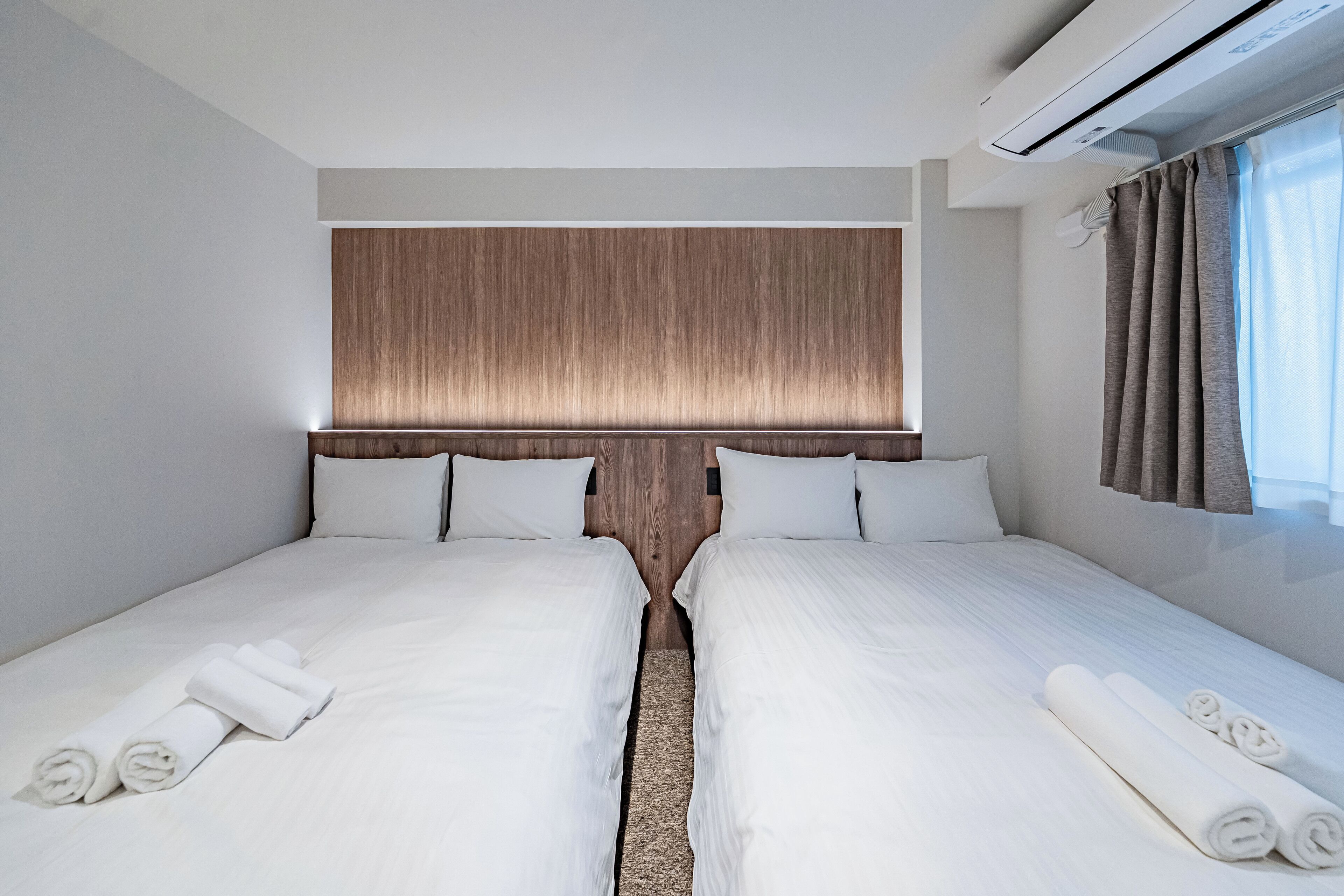 A hotel room with two beds, a wooden headboard, white linens, and a window with curtains.