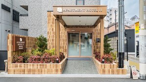Der Eingang zum Apartment Hotel 11 mit einer gefliesten Fassade, einer Glastür und einem kleinen Garten mit roten Blumen.