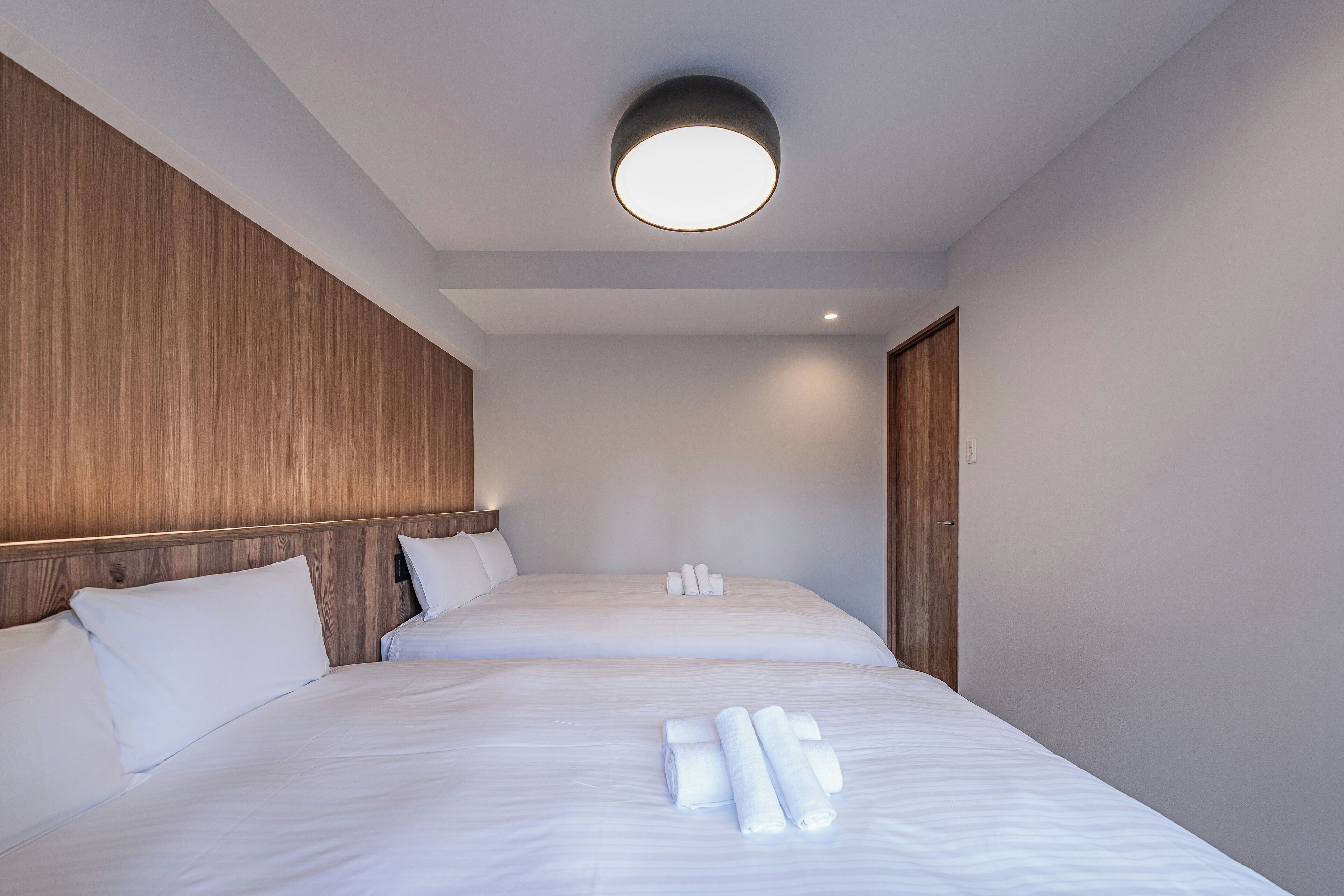 A hotel room with two beds, wooden headboards, white linens, and a round ceiling light.