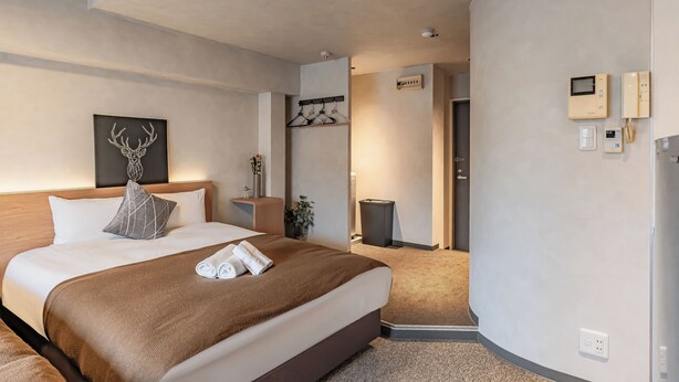 Ein modernes Hotelzimmer mit einem großen Bett, Nachttischen, einem Kleiderständer und Blick auf den Flur.