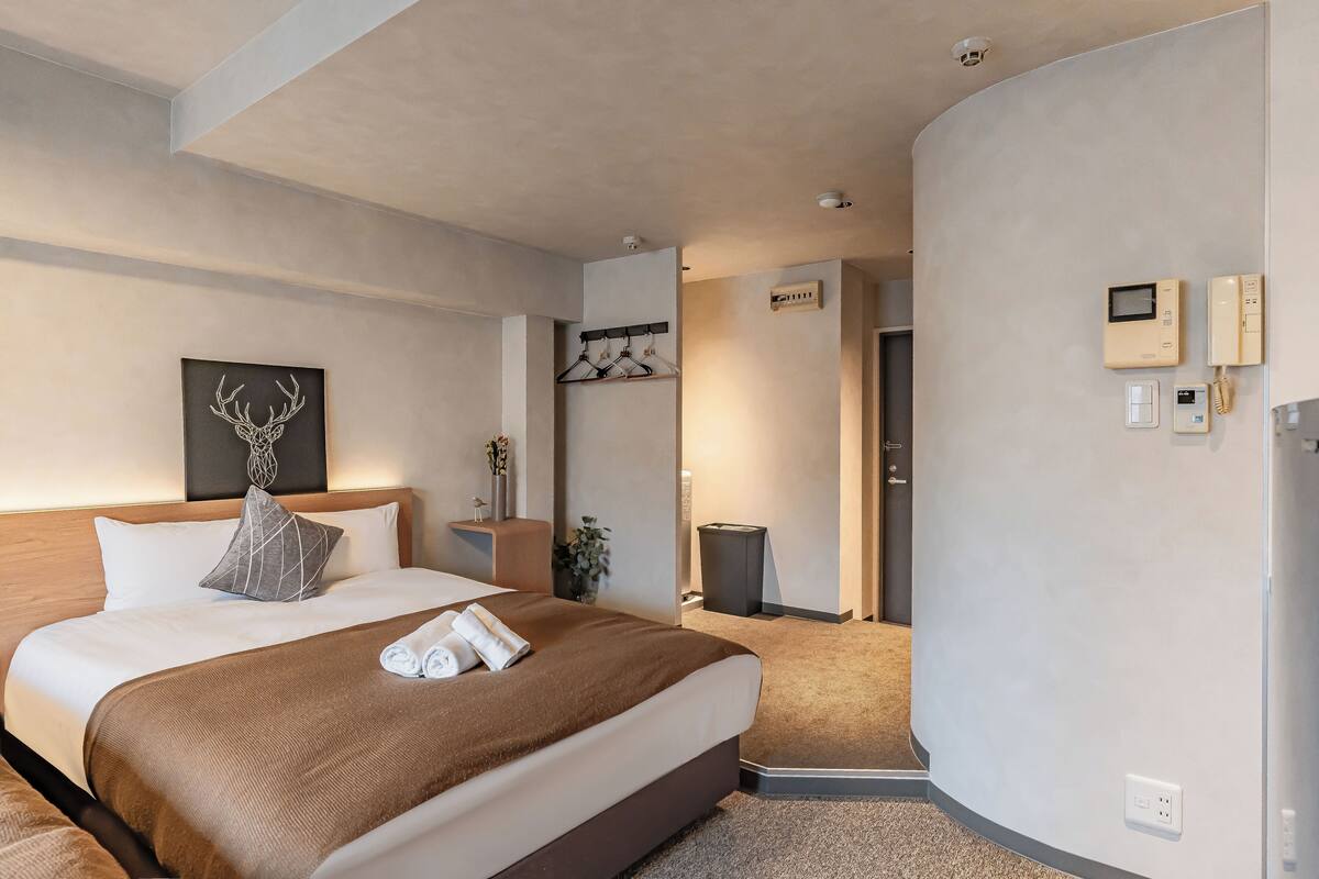 A modern hotel room with a large bed, bedside tables, a coat rack, and a view of the hallway.