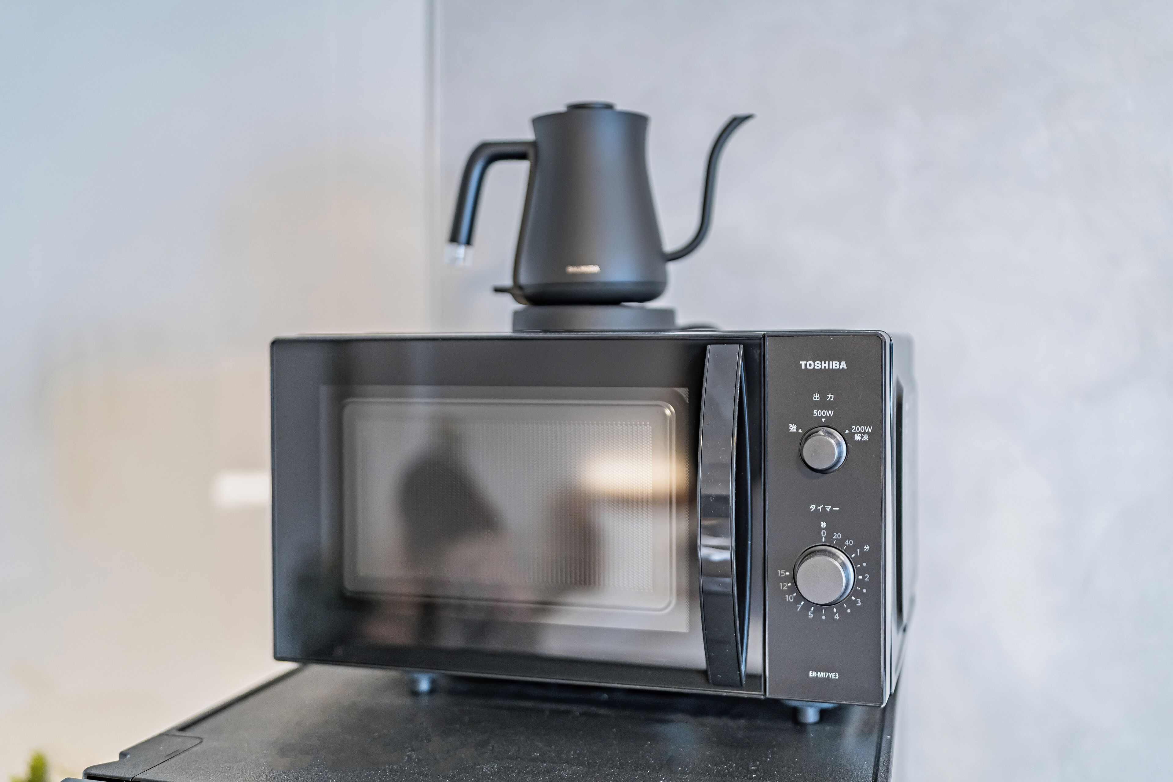 Une cuisine moderne avec un micro-ondes noir et une cafetière posée sur le plan de travail.
