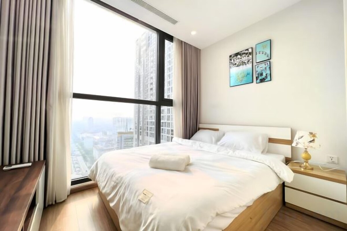 A hotel room with a large bed, a bedside table, a nightstand, and a window with curtains.