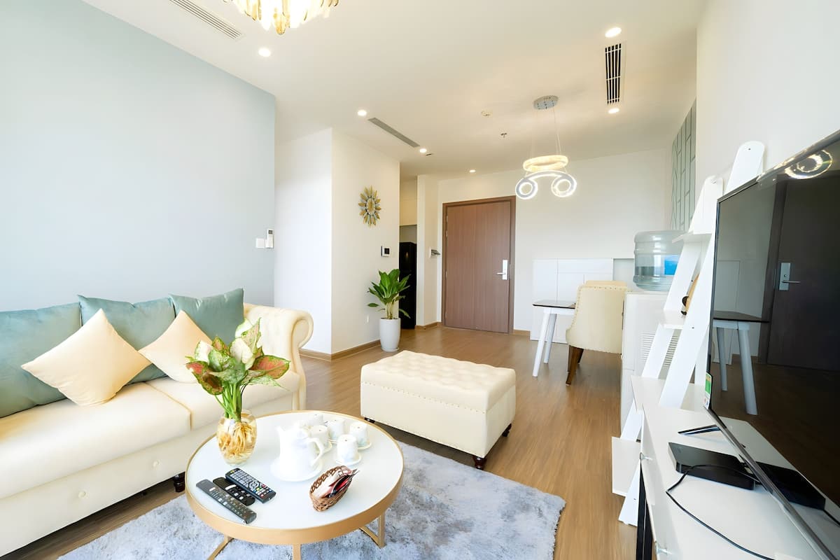 A modern living room with a sofa, coffee table, and TV. There is a dining area with a table and chairs.