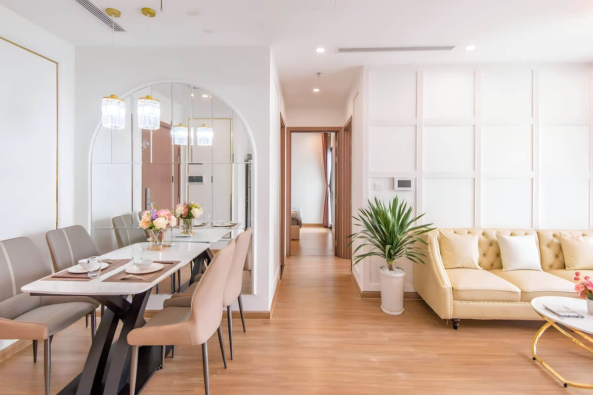 A modern living room with a sofa, a dining table with chairs, and a large mirror.