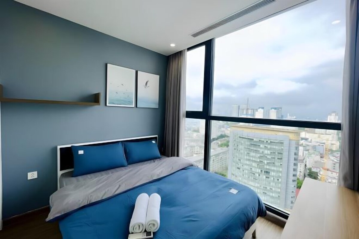 A modern hotel room with a large bed, a city view, and a minimalist design.
