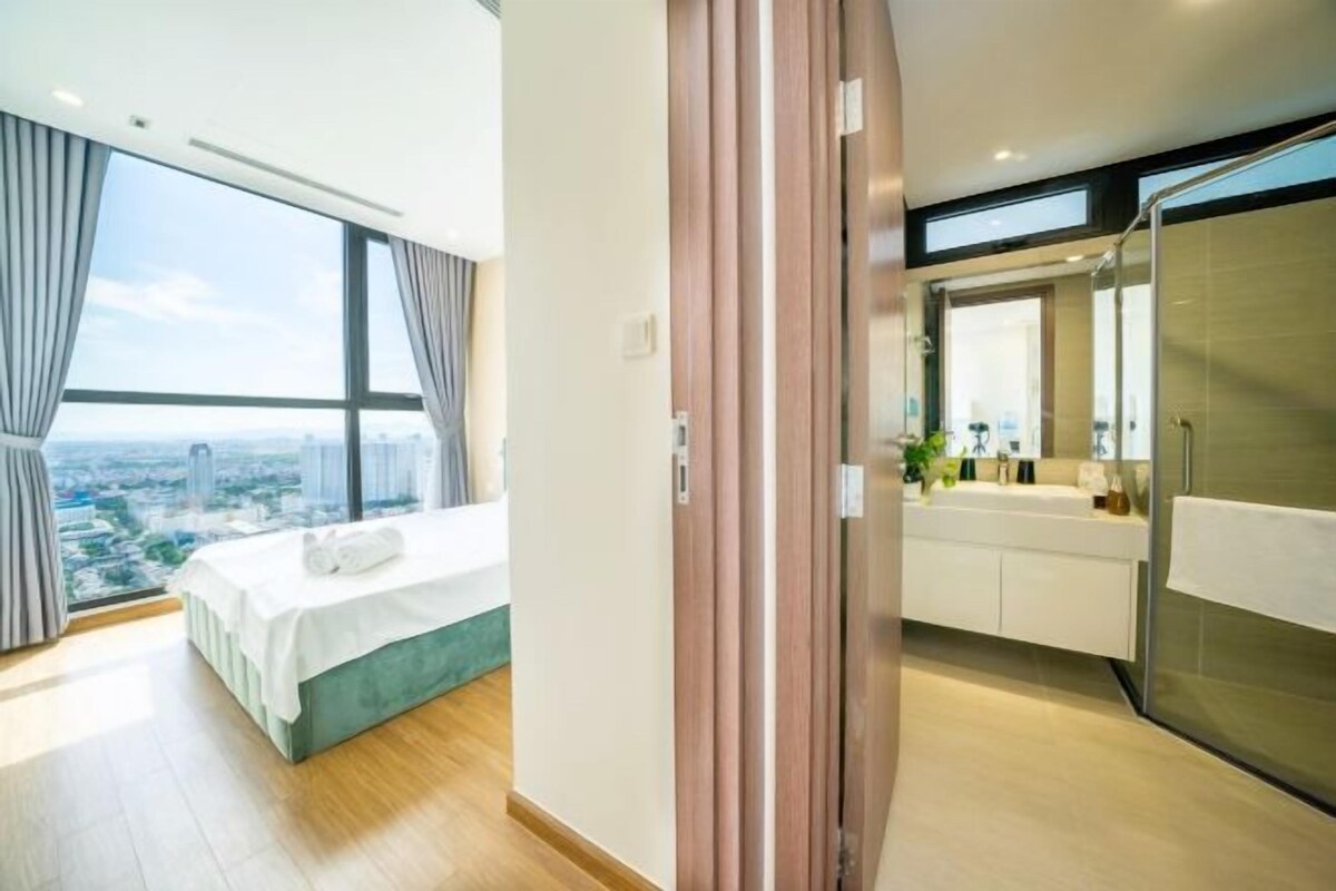 A modern hotel room with a large bed, a bathroom with a glass shower, and a city view.