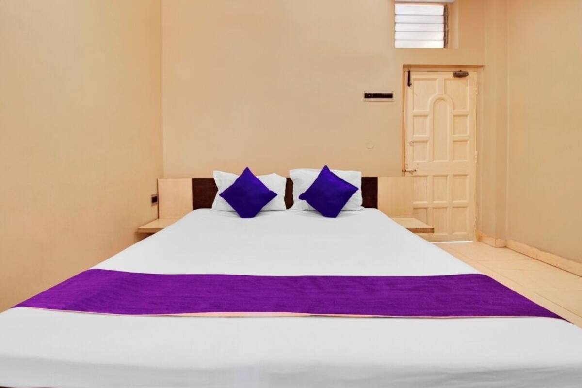 Una habitación de hotel con una cama grande, dos mesitas de noche, una puerta y un ventanal pequeño.