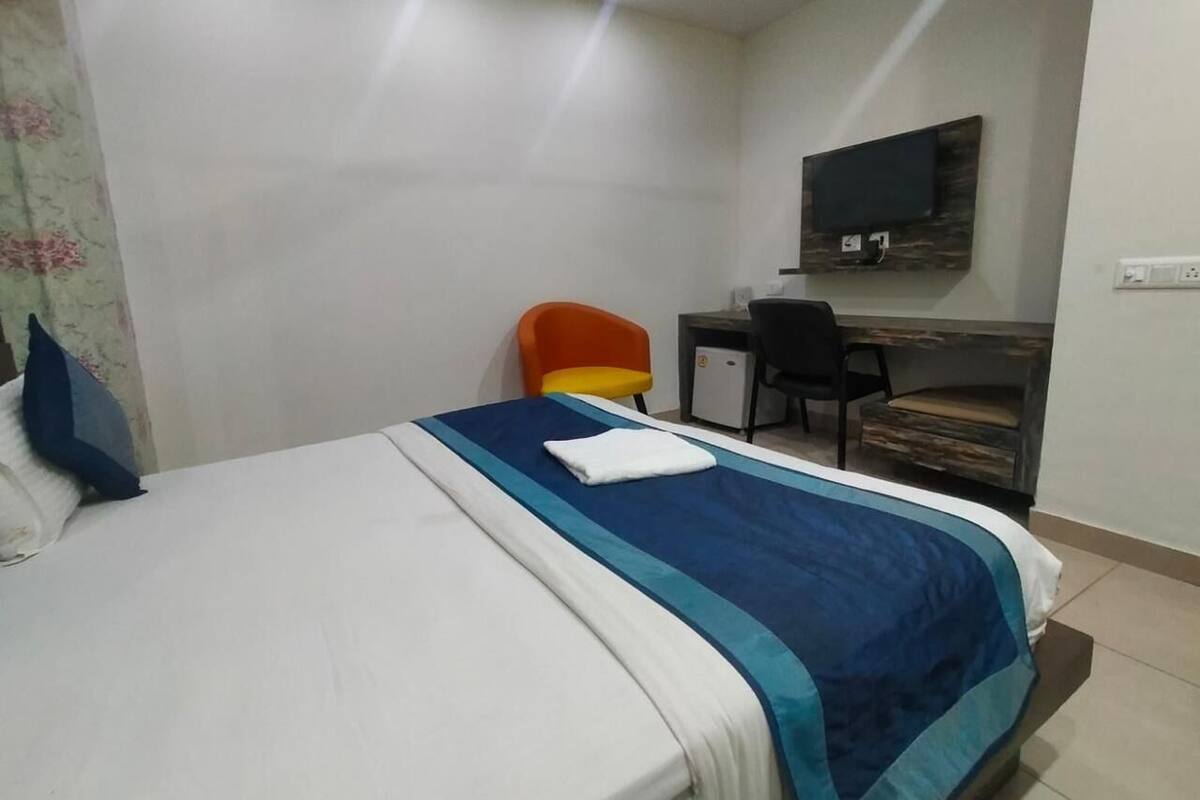 Ein Hotelzimmer mit einem Bett, einem Schreibtisch, einem orangefarbenen Sessel und einem an der Wand befestigten Fernseher.