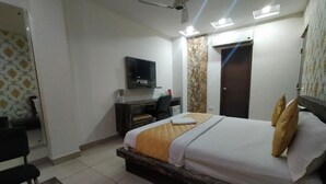 A bedroom with a bed, a desk, a chair, a TV, and a wardrobe. - Hotel Maya Inn (Noida)
