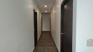 A narrow hallway with tiled flooring, white walls, and dark wooden doors. - Hotel Maya Inn (Noida)