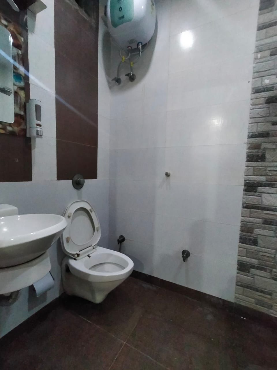 A bathroom with a toilet, sink, and a hand dryer mounted on the wall.