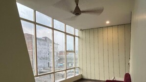 A spacious room with large windows, a red sofa, and a ceiling fan. - Hotel Maya Inn (Noida)