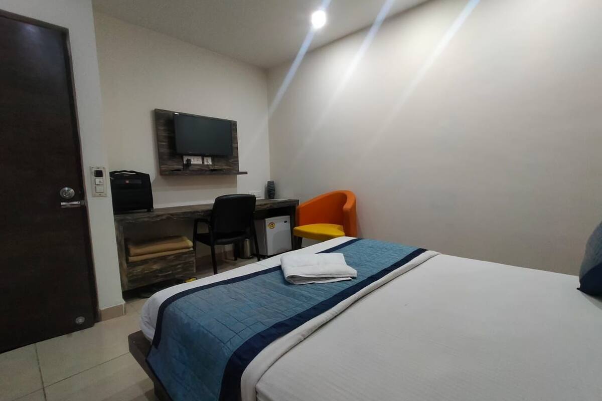 Ein Hotelzimmer mit einem Bett, einem Schreibtisch, einem Sessel und einem an der Wand befestigten Fernseher.