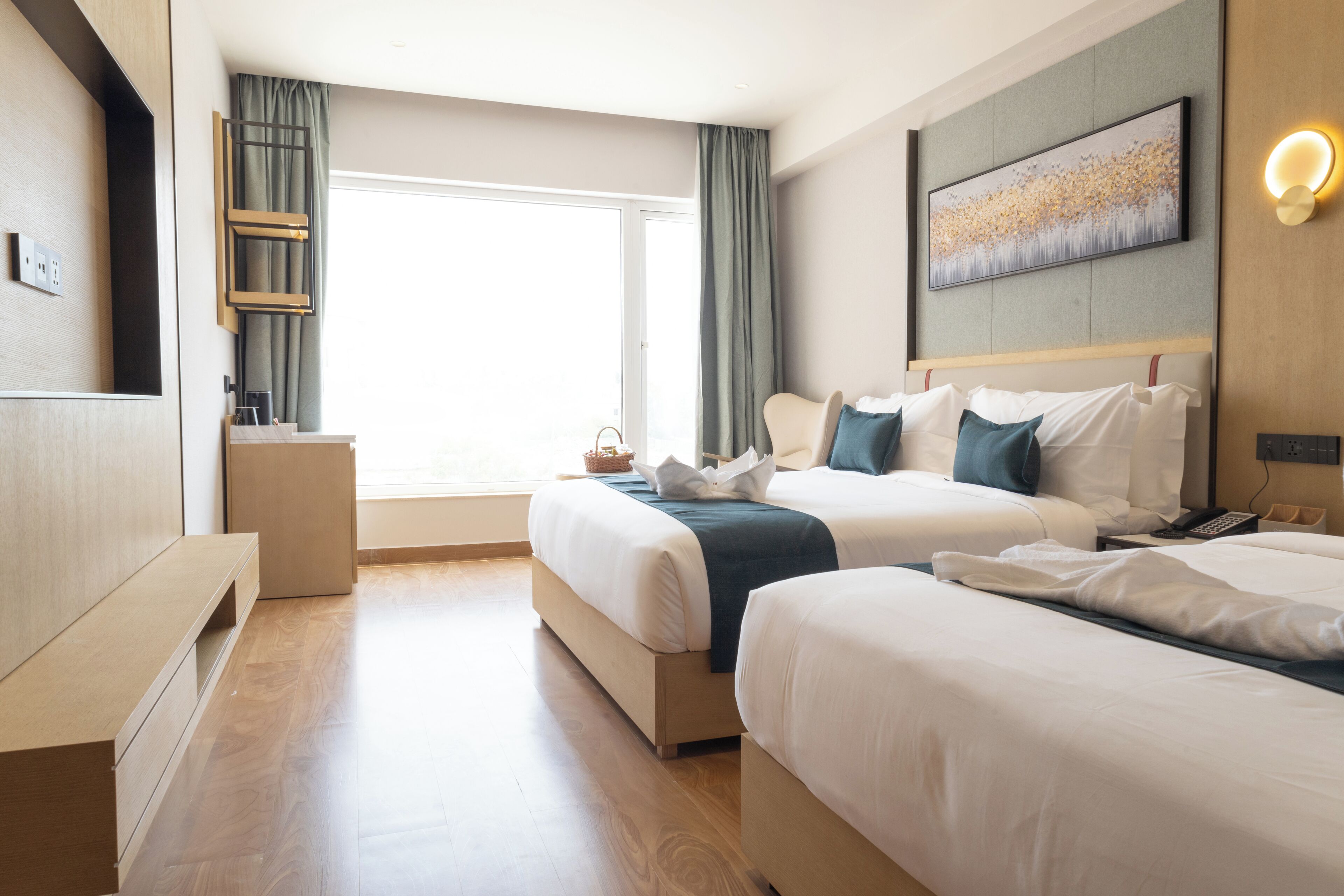 Ein Hotelzimmer mit zwei Betten, einem großen Fenster, einem Bild an der Wand und einem Nachttisch.