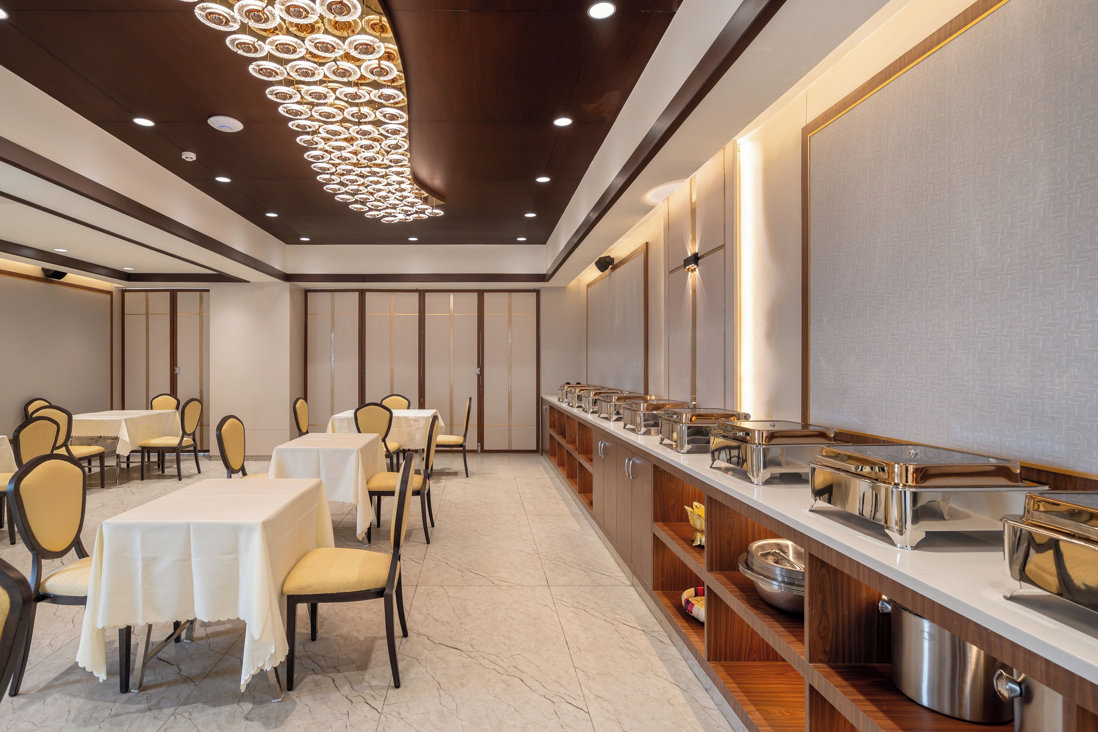 Een hotel eetruimte met tafels en stoelen, een buffet en een decoratieve plafondlamp.