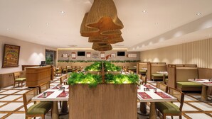A restaurant with wooden tables and chairs, a central planter with greenery, and a ceiling light fixture. - Copper Leaf Hotels, Tirunelveli (Palayankottai)