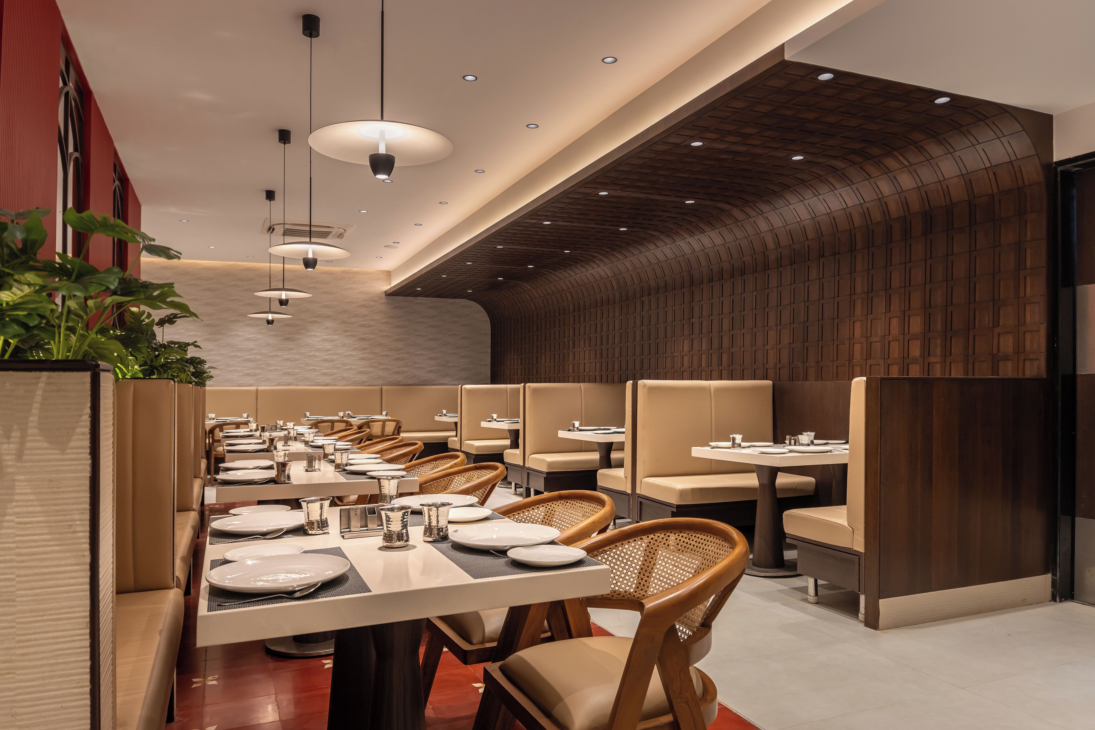 A modern restaurant with long communal tables, cushioned booths, and pendant lighting.