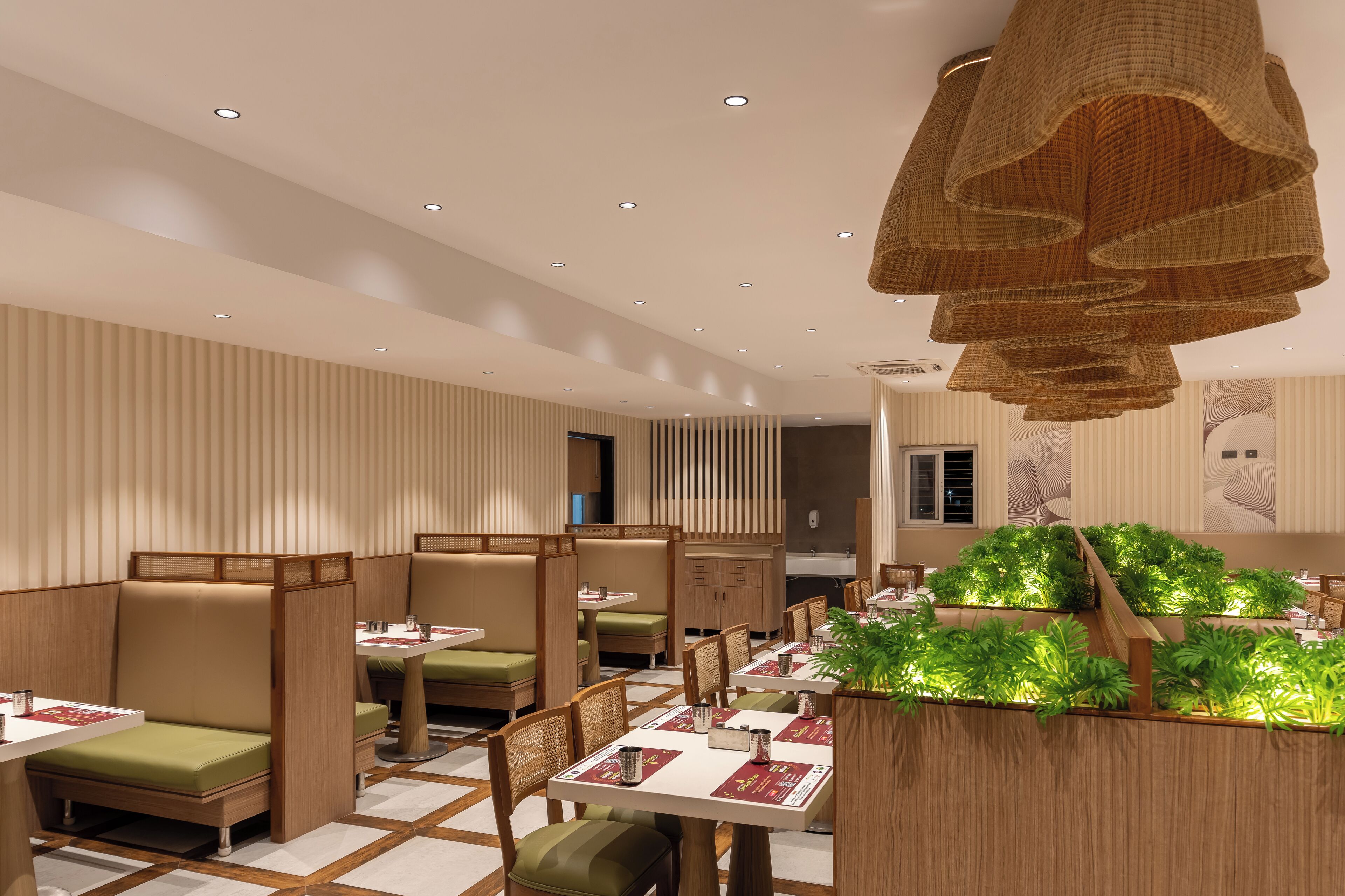 Interior de restaurante moderno con asientos tipo cabina, detalles de madera y plantas verdes.