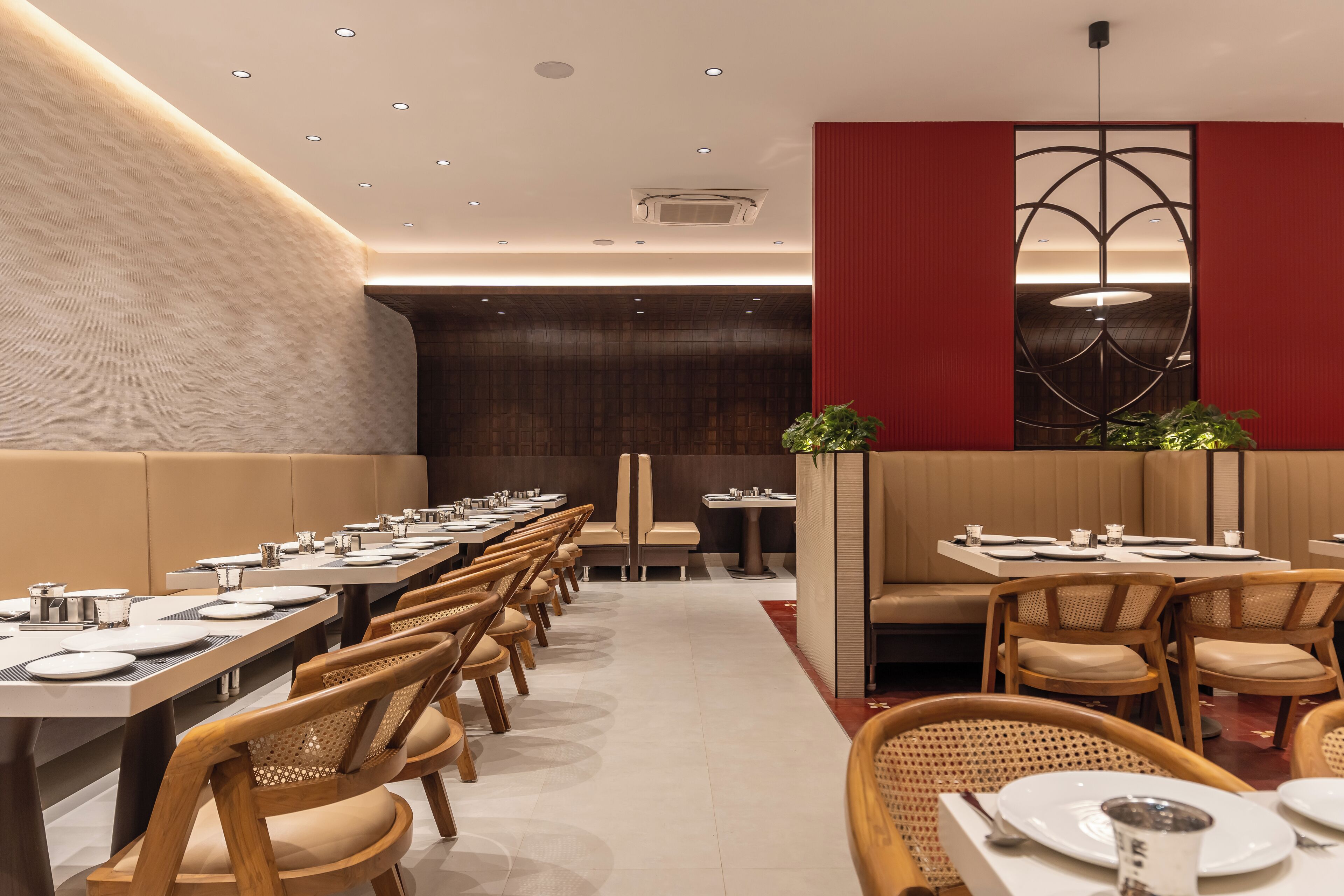 A modern restaurant with long communal tables, cushioned booths, and a contemporary ceiling design.