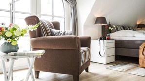 Et moderne soveværelse med en brun lænestol, et natbord med en lampe, en seng med stribet sengetøj og et vindue med gardiner.