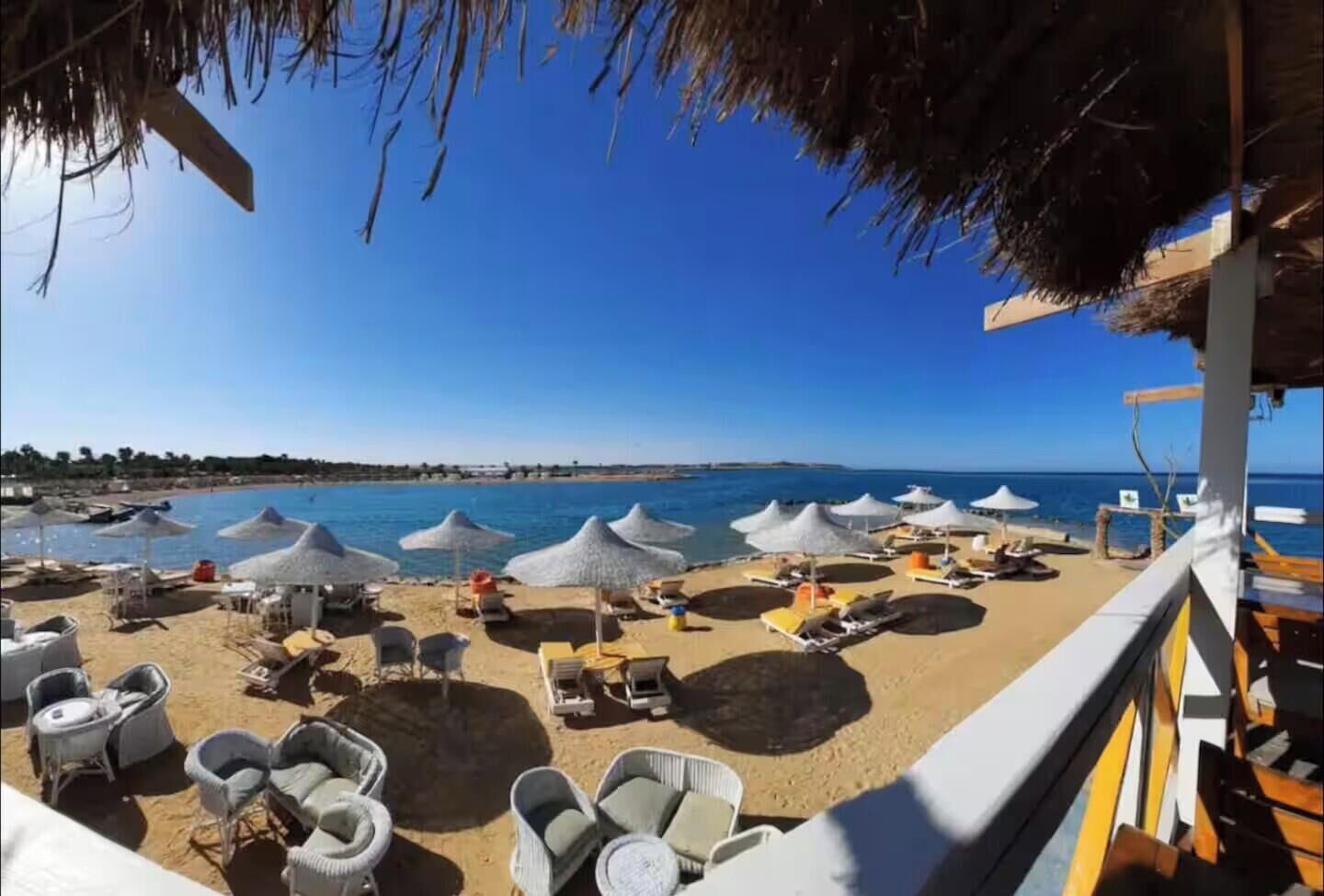 Blick auf einen Strand mit Sonnenschirmen, Liegestühlen und blauem Himmel.