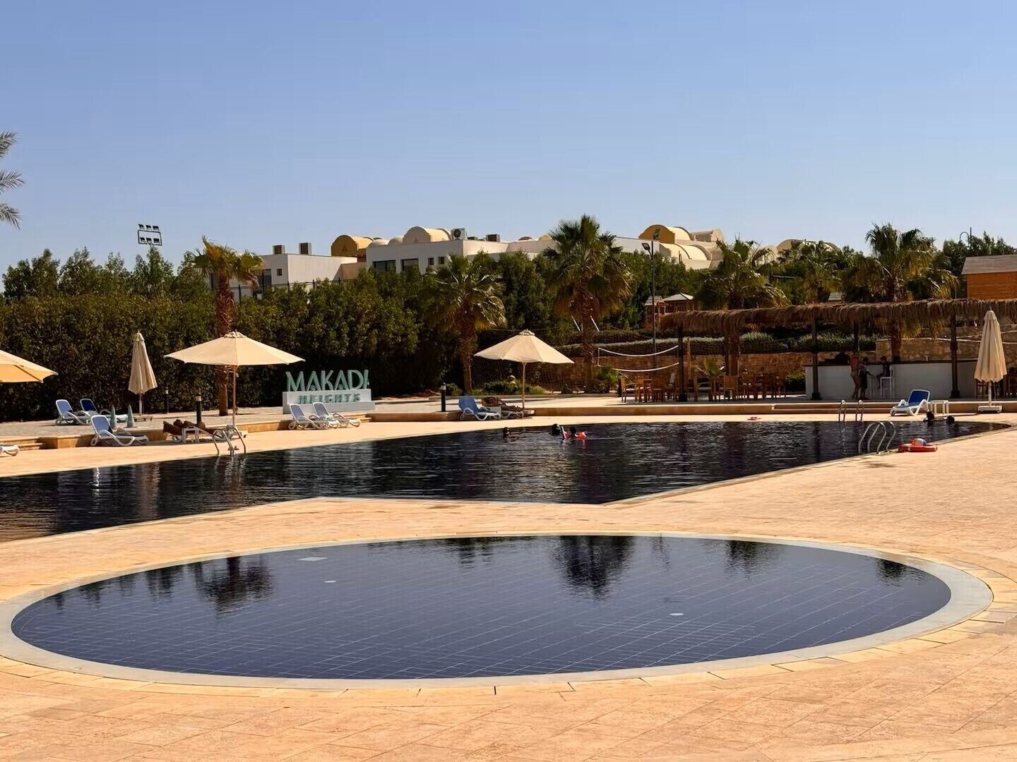 A pool area with lounge chairs, umbrellas, and a sign for 'MAKADI HEIGHTS'.